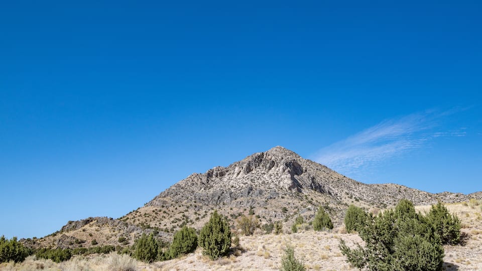 A mountain with sparse vegetation and a clear blue sky.