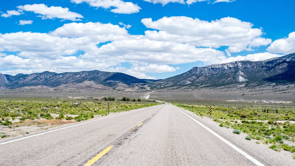 A straight road with mountains in the distance under a clear blue sky.