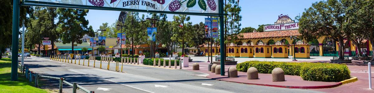Une enseigne indiquant l’entrée de Knott’s Berry Farm, avec un ciel bleu clair et un bâtiment jaune en arrière-plan.