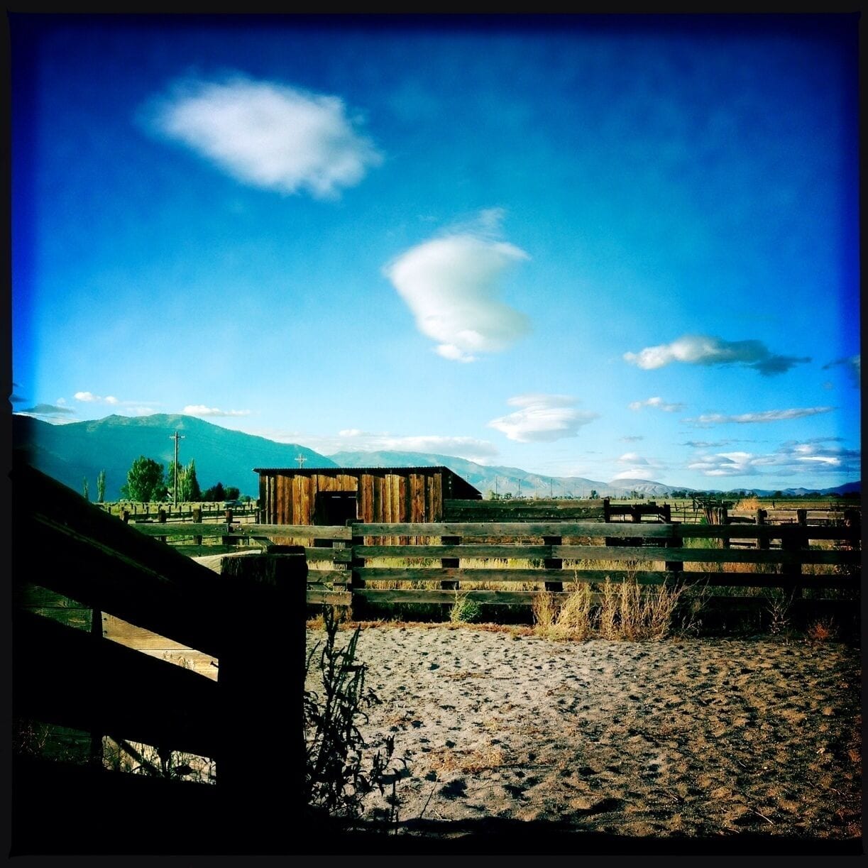 A wooden barn in a rural landscape with mountains in the background.