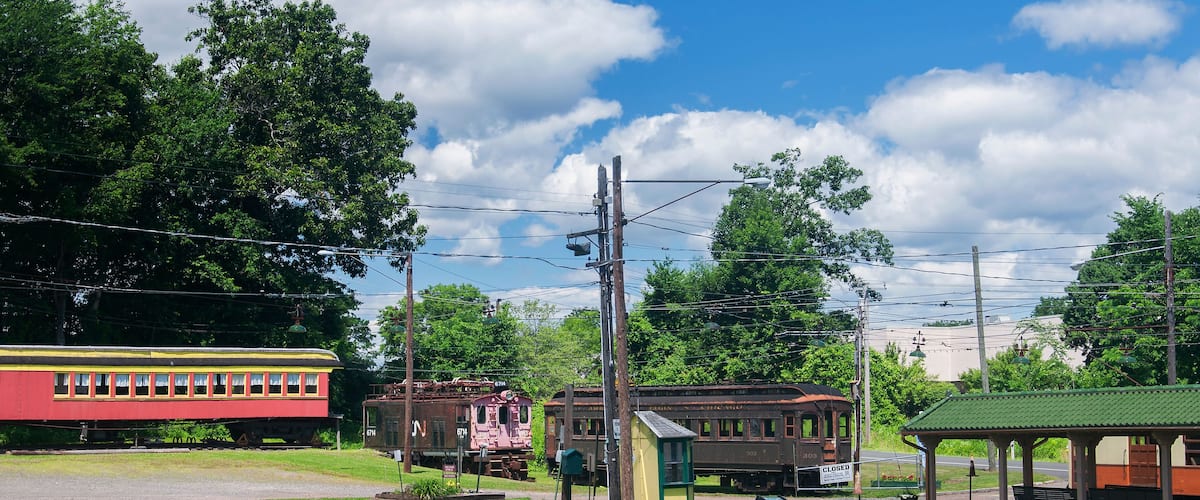 A vintage train station with a red train, a caboose, and a small shelter.