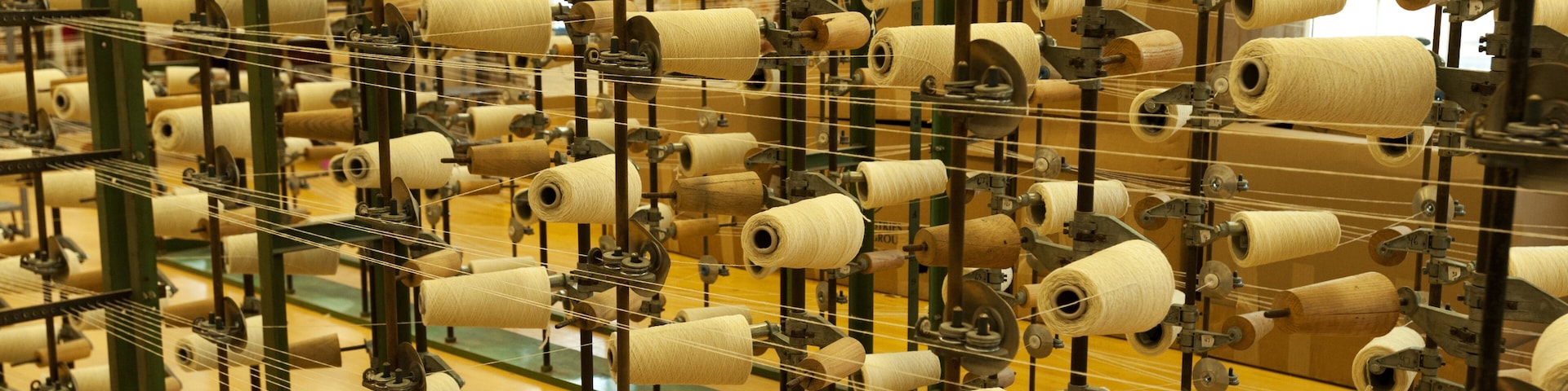 Uma fábrica têxtil com inúmeros carretéis de linha em prateleiras verticais e horizontais.
