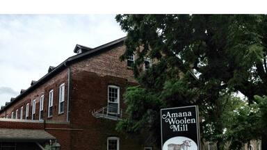 Um edifício de tijolos com uma placa que diz 'Amana Woolen Mill, Operating since 1857'.