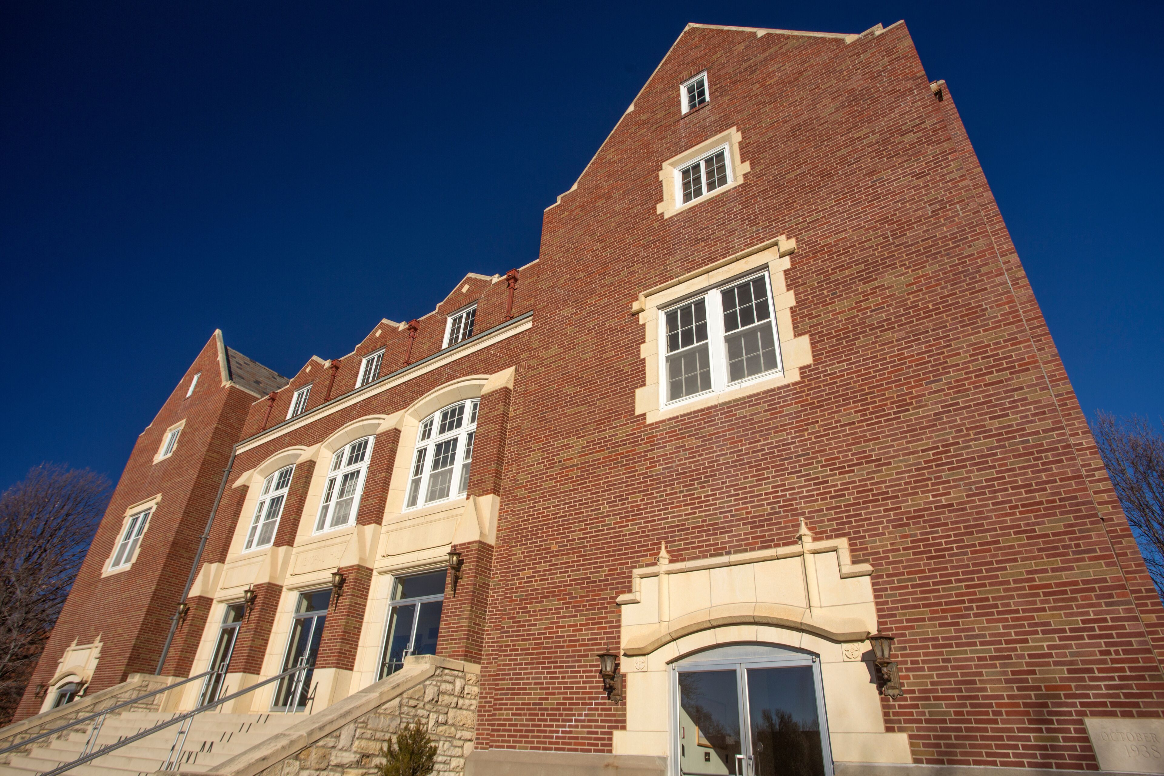 A red brick building with a stone staircase, large windows, and a clear blue sky.