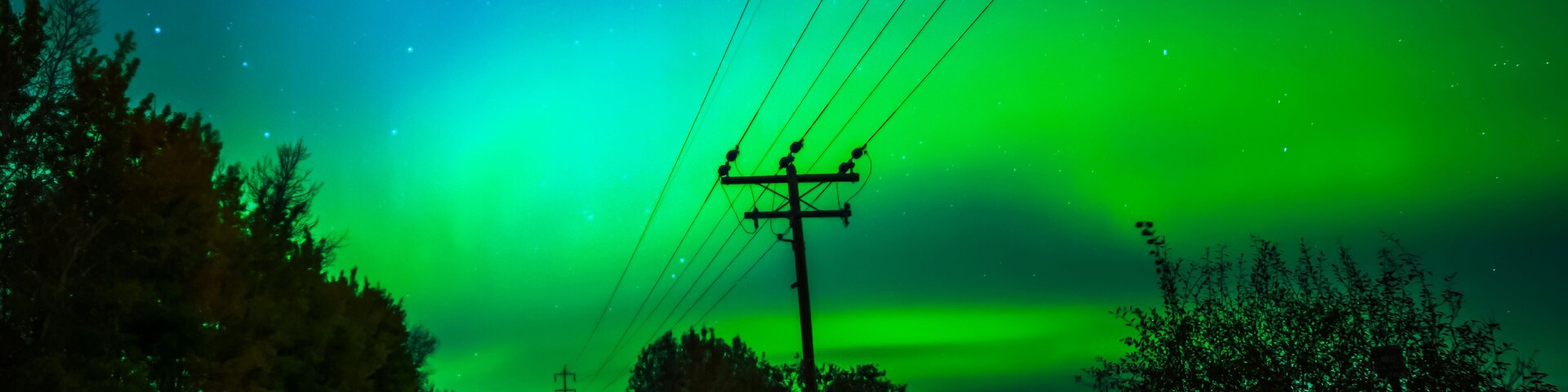 Northern Lights glowing green in the starry sky above a rural road and transmission lines, Sturgeon County; Alberta, Canada