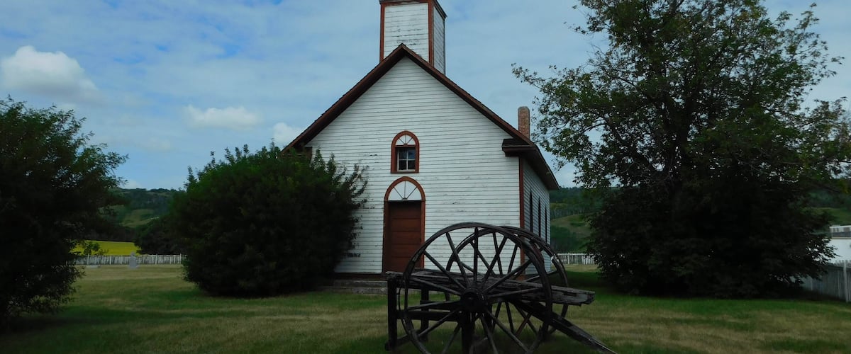 A white church with a bell tower and a large wooden wheel in front.