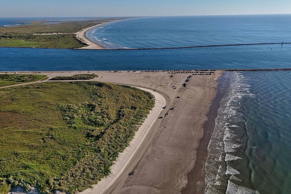 Vue aérienne d’une zone côtière comprenant une plage, une digue et une route qui longe la côte.