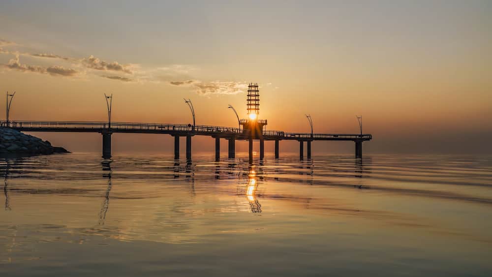 Un pont doté d’une tour centrale qui reflète le coucher de soleil sur une étendue d’eau calme.