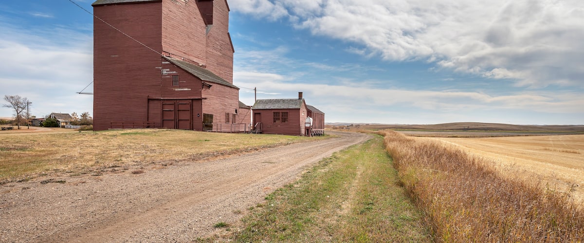 A large red grain elevator in a rural landscape with a dirt road leading to it.