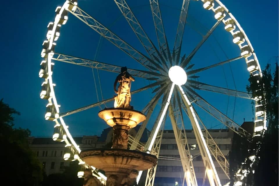 A large Ferris wheel with a central fountain at night.