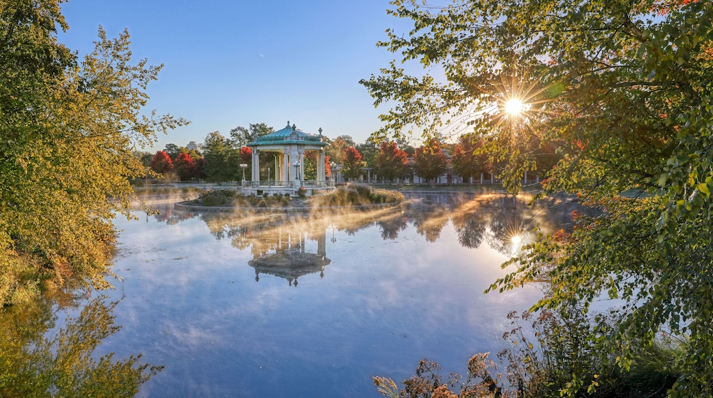 A gazebo by a calm lake with autumn foliage and a clear sky.