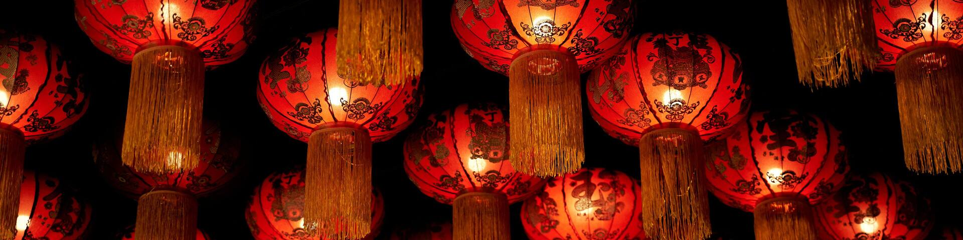 A collection of red lanterns with golden tassels hanging against a dark background.