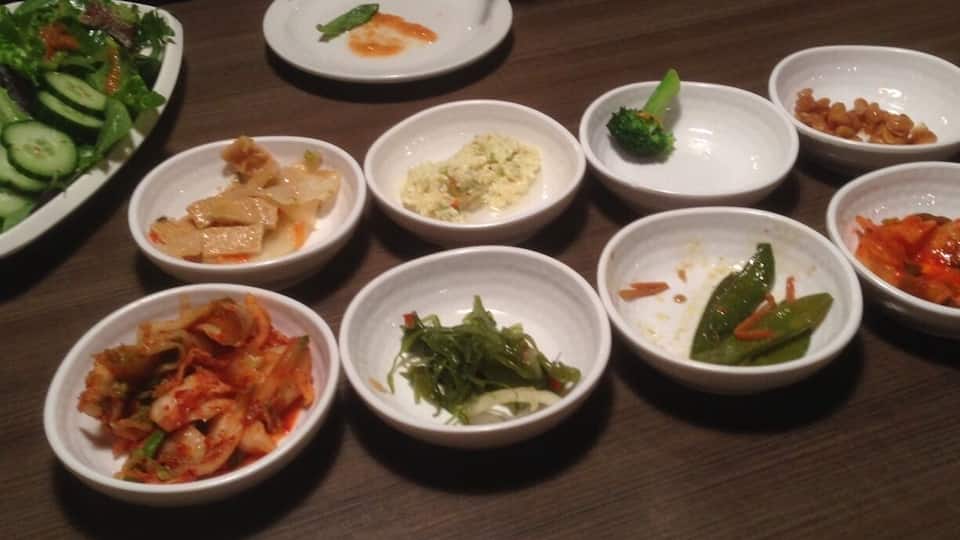 A table with various small dishes of food, including kimchi, vegetables, and other Korean dishes.