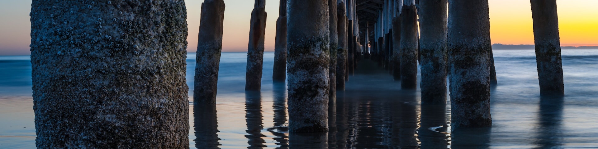 Muelles de madera y pilares de piedra se adentran en aguas tranquilas durante el atardecer.