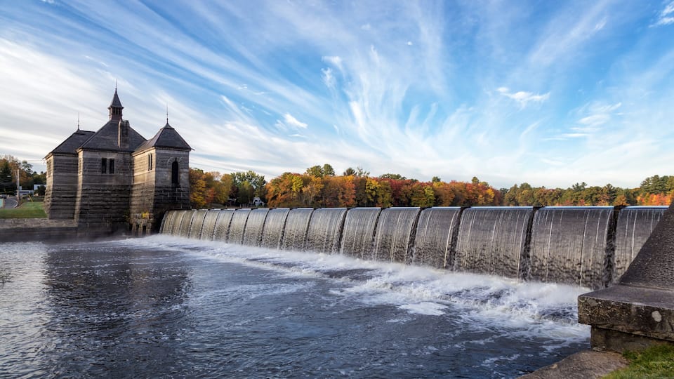 A dam with a water spillway and a stone building with a pointed roof.