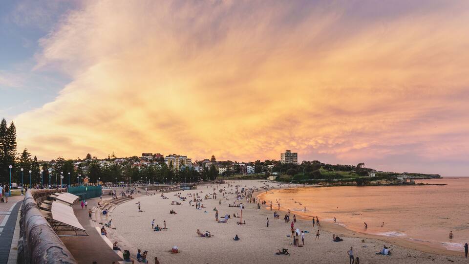 A beach with people, a sunset, and buildings in the background.