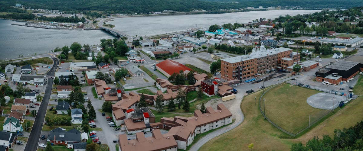 An aerial view of a town by a river with a bridge, buildings, and green hills in the background.