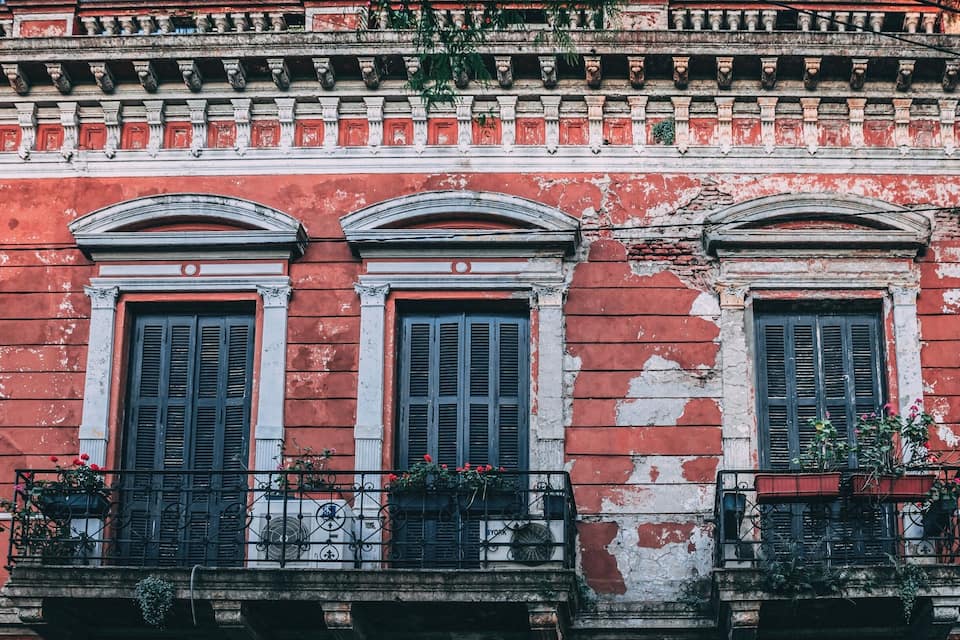 A red building with three windows and balconies with plants.