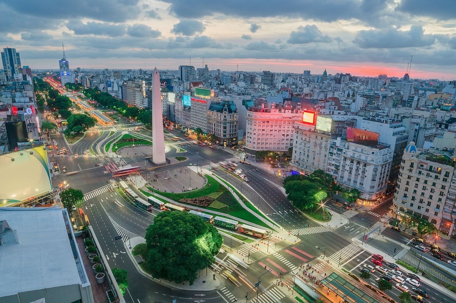 Un paisaje urbano con un monumento destacado, calles concurridas y edificios modernos.