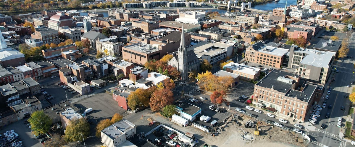 An aerial view of a city with a prominent church steeple, a river, and autumn foliage.