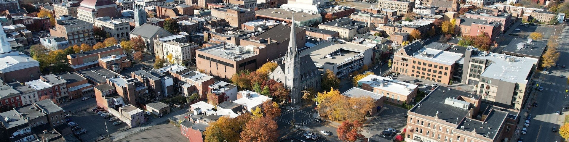 An aerial view of a city with a prominent church steeple, a river, and autumn foliage.