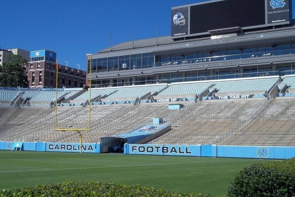 Um estádio de futebol com arquibancadas vazias, um placar e o logotipo da Universidade da Carolina do Norte.