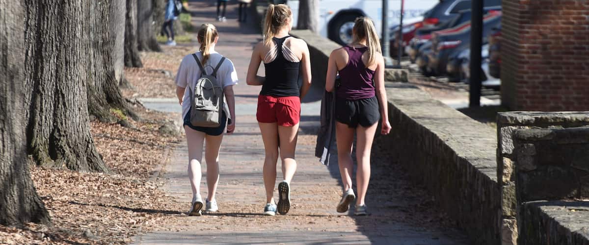3 attractive college girls in athletic clothing walk near campus