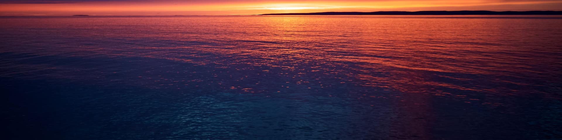 A sunset over a calm sea with a horizon line.