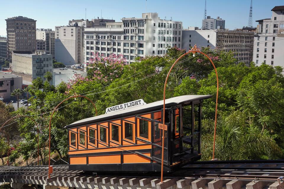 Une télécabine portant l’inscription « Angels Flight » circule sur des rails, avec une vue sur la ville en arrière-plan.