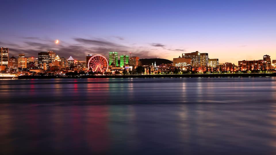 A city skyline at dusk with illuminated buildings and a prominent Ferris wheel.