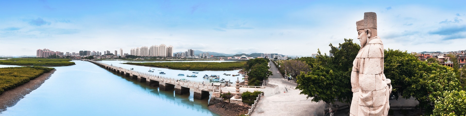 A river with a bridge, a statue, and a cityscape in the background.