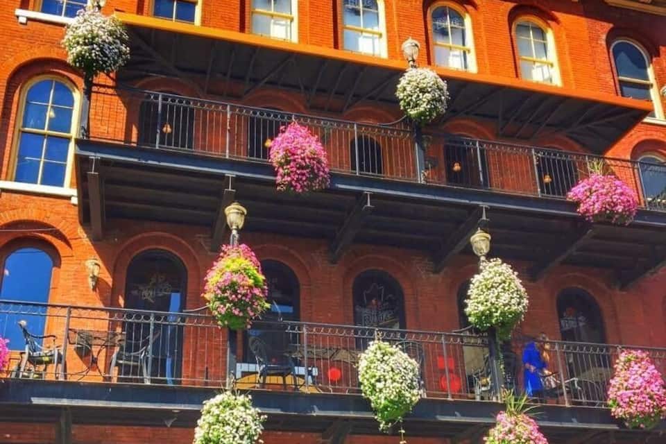 A red brick building with multiple balconies adorned with hanging flower baskets.