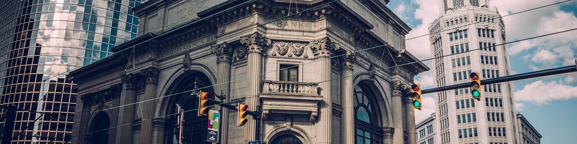 A historic bank building with a prominent clock, surrounded by modern skyscrapers.