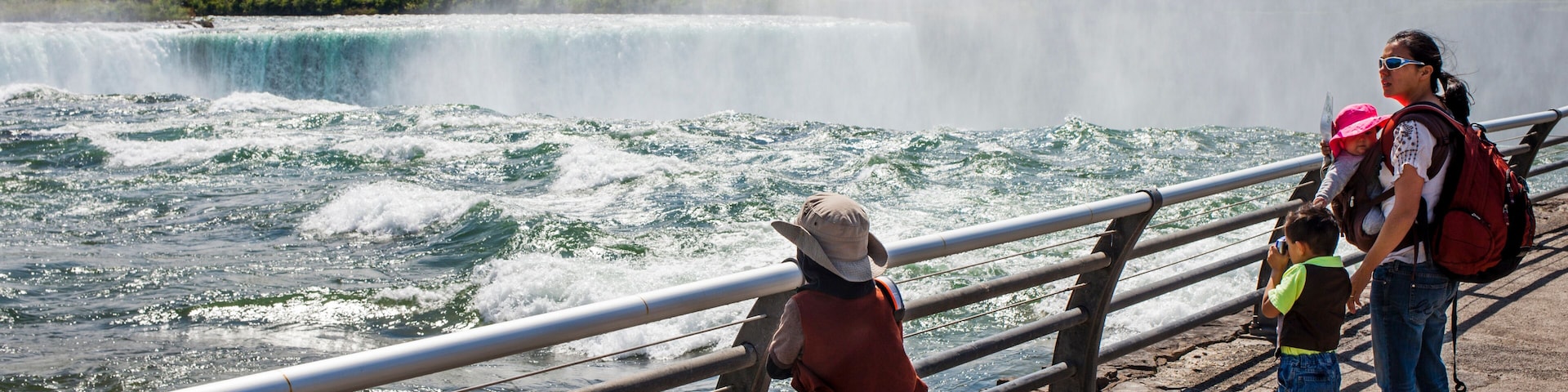 Mother standing beside Niagara Falls barrier with two little sons and baby daughter