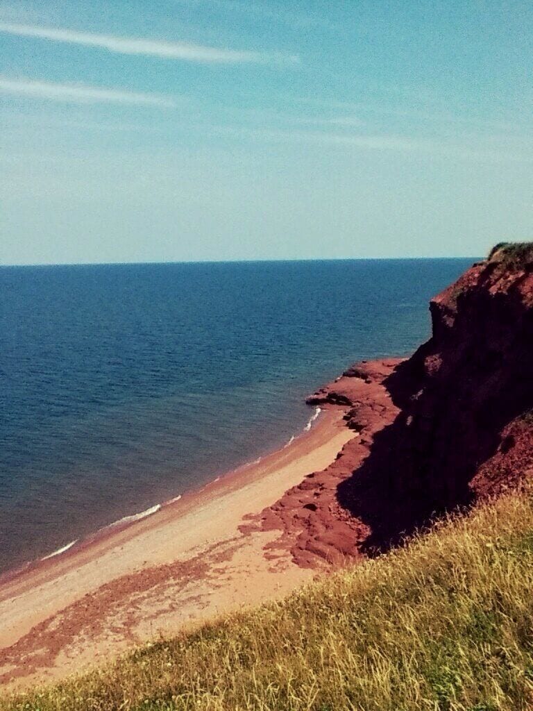 A coastal landscape with a sandy beach, a rocky cliff, and the ocean.