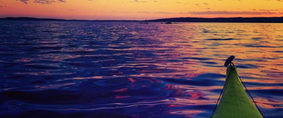 A sunset over a body of water with a green boat in the foreground.