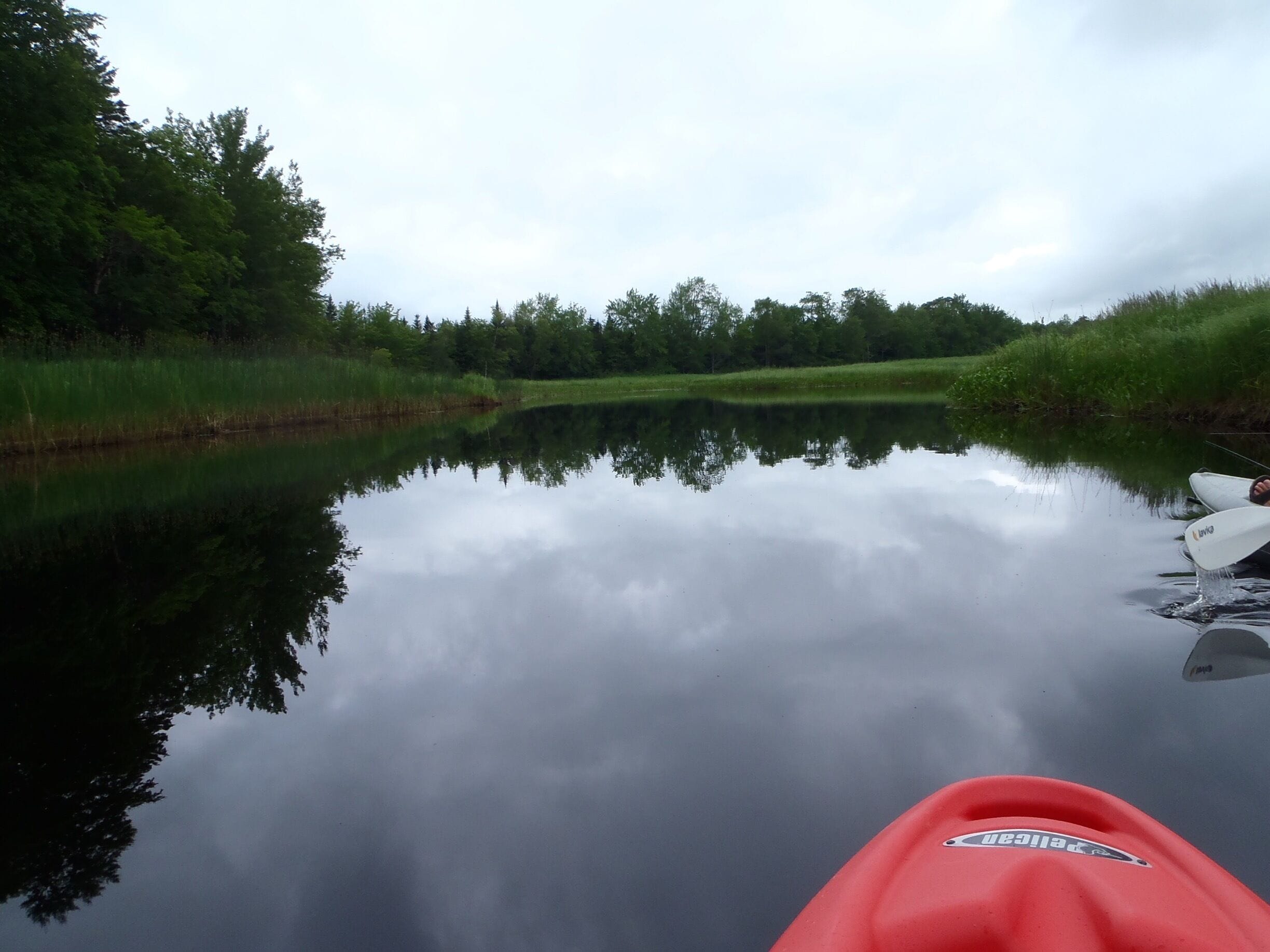 A calm river with a red kayak and a white boat on the right bank.