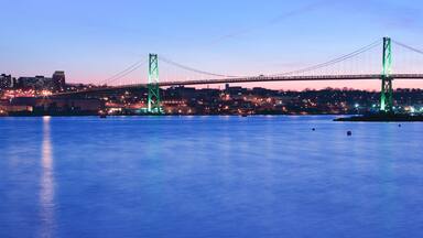 A bridge spanning a body of water with city lights in the background.