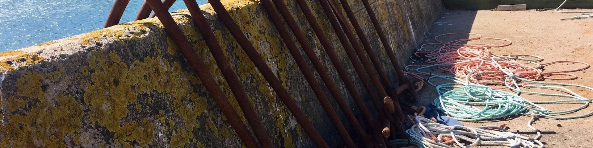 A concrete pier with rusted metal railings and colorful ropes.