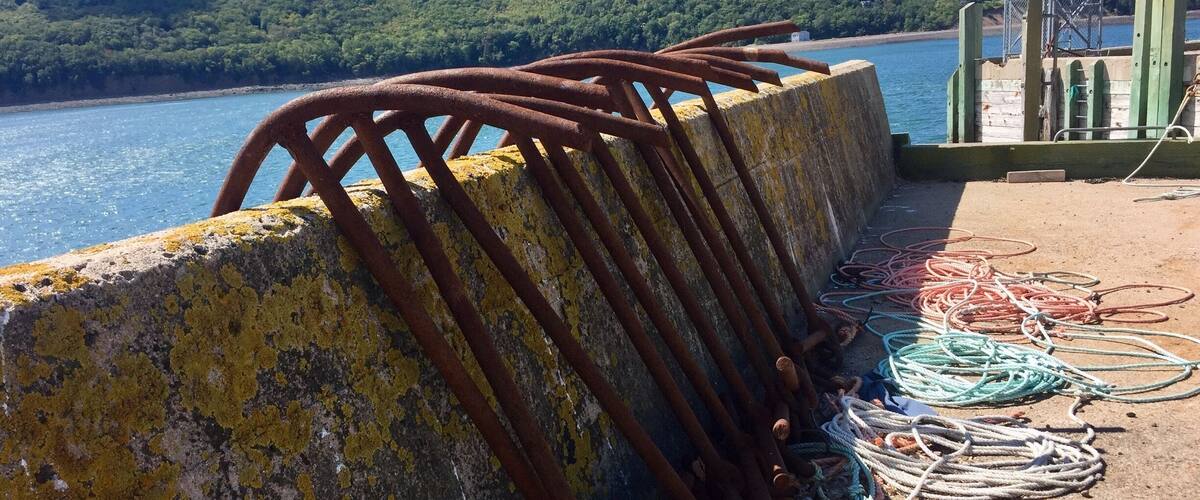 A concrete pier with rusted metal railings and colorful ropes.