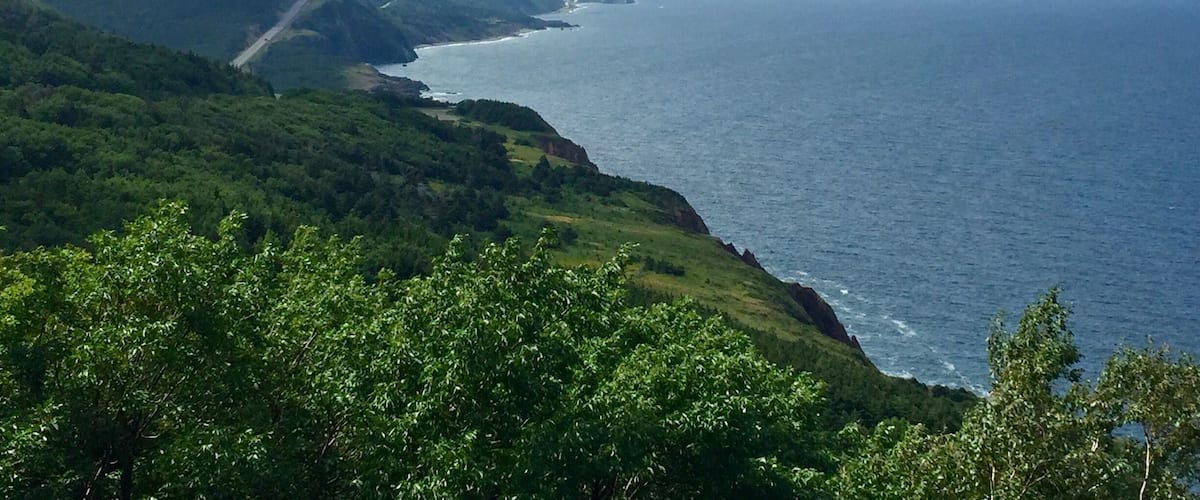 A coastal landscape with a winding road along the cliffs, a view of the ocean, and lush green hills.
