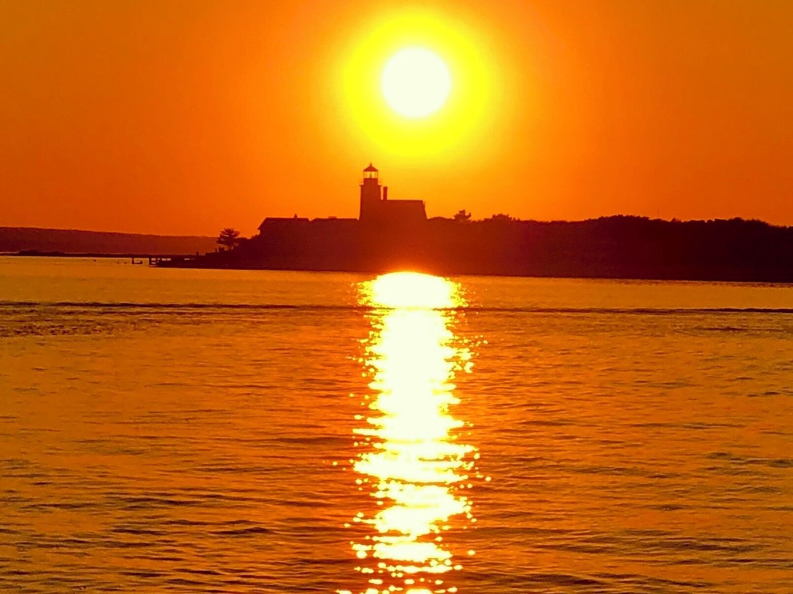 A sunset over a body of water with a lighthouse silhouette on a distant hill.
