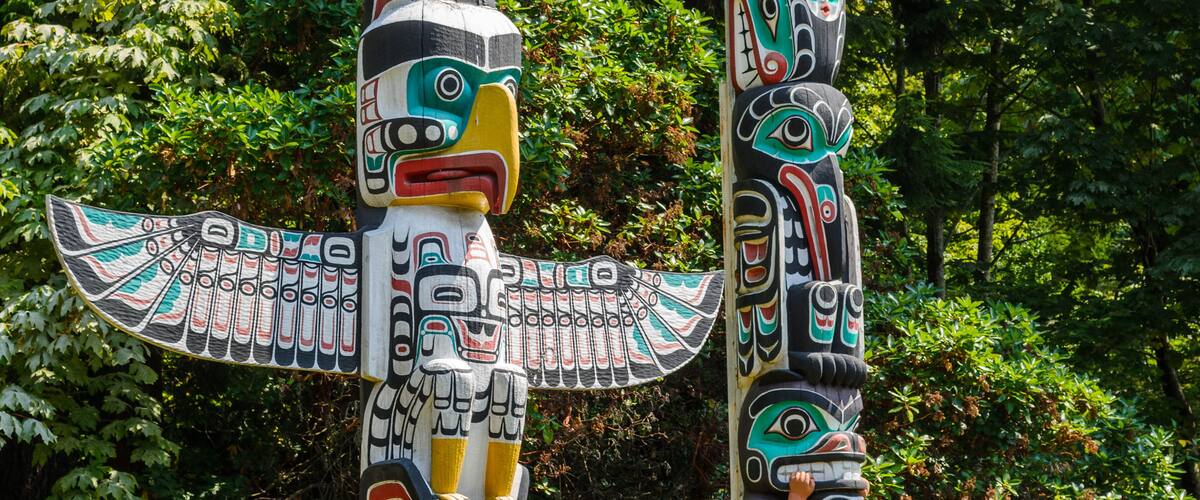 Totem poles with intricate designs and a dense forest background.