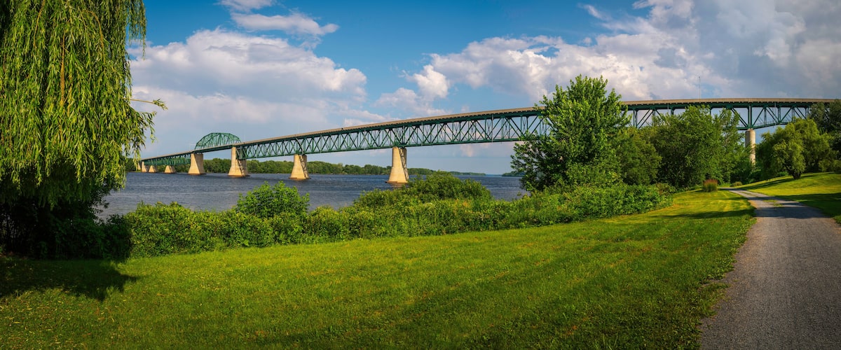 A green metal bridge over a river, surrounded by lush greenery and a clear sky.