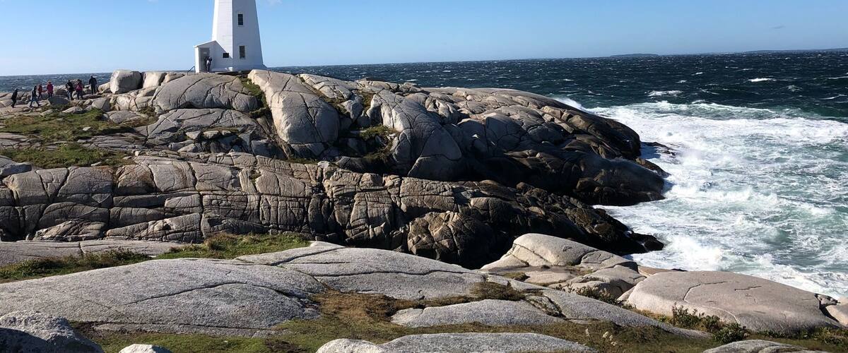 A white lighthouse with a red top on rocky terrain by the sea.
