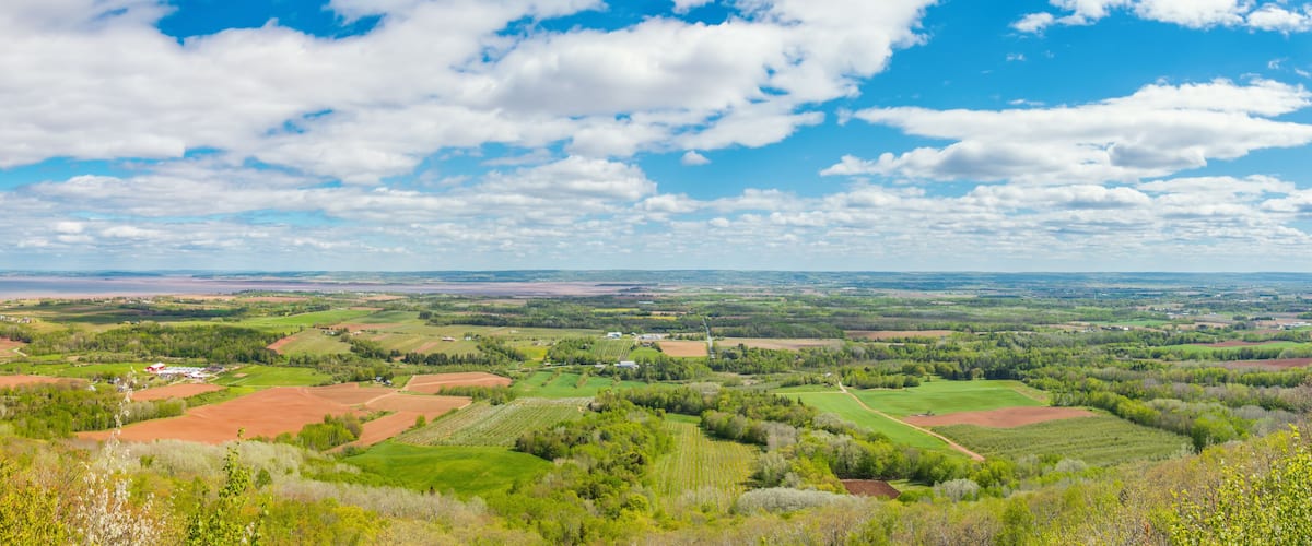 A rural landscape with fields, trees, and scattered buildings under a partly cloudy sky.
