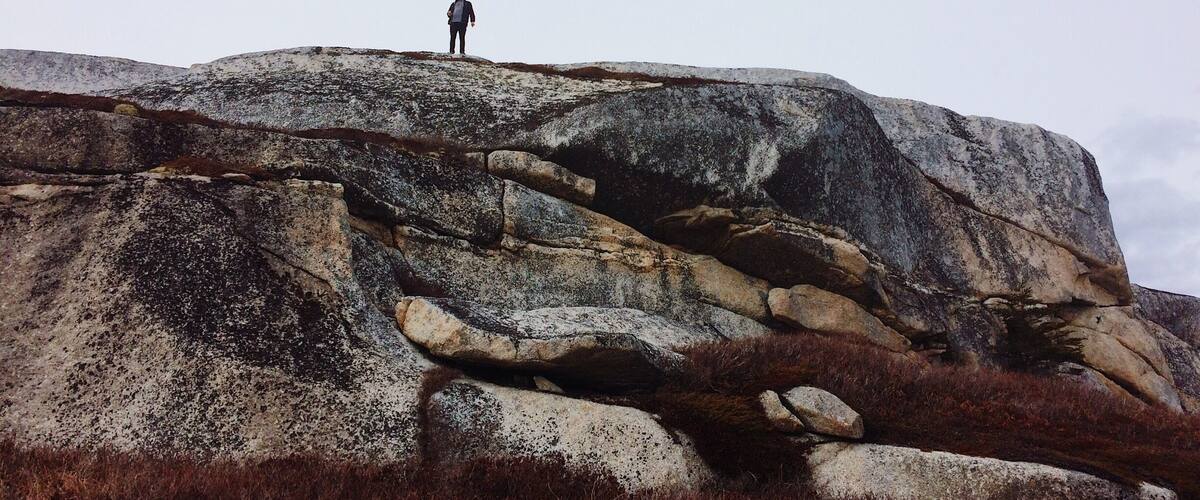 A person standing on a large rock formation with sparse vegetation.