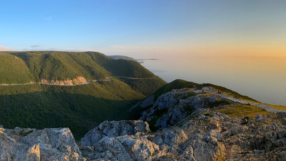 A mountainous landscape with a winding road, a wooden walkway, and a sunset over a body of water.