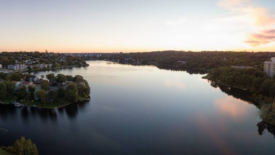 A calm river surrounded by residential areas and trees, with a sunset in the background.