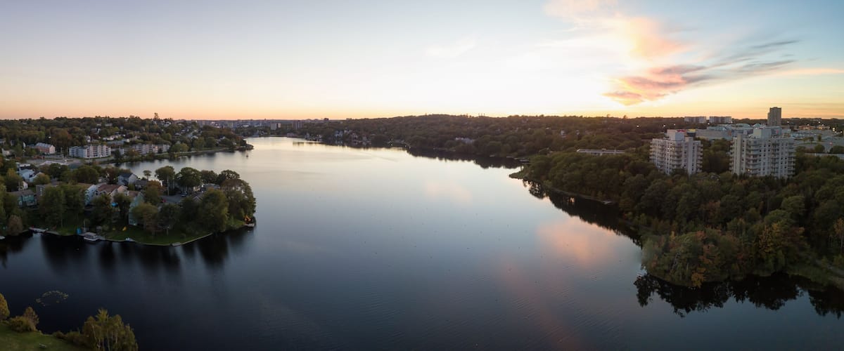 A calm river surrounded by residential areas and trees, with a sunset in the background.